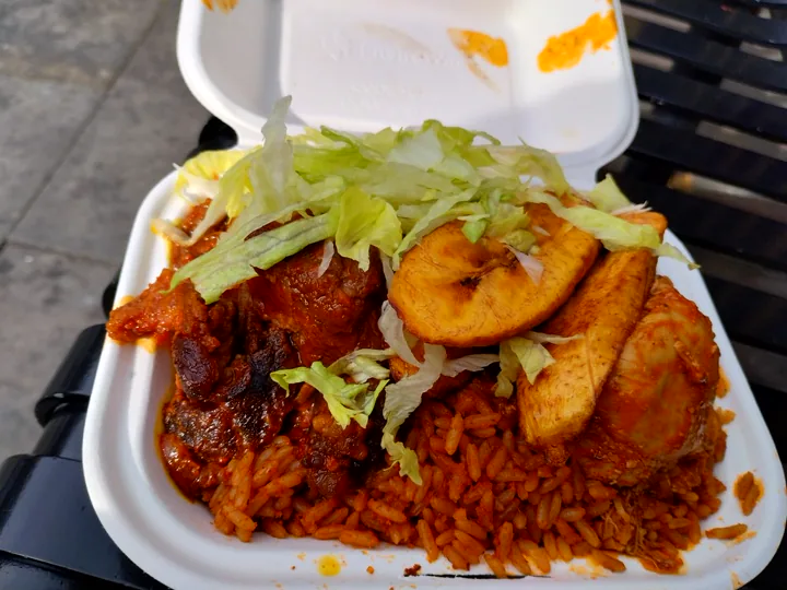 A plate of jollof rice served with fried plantain and stew