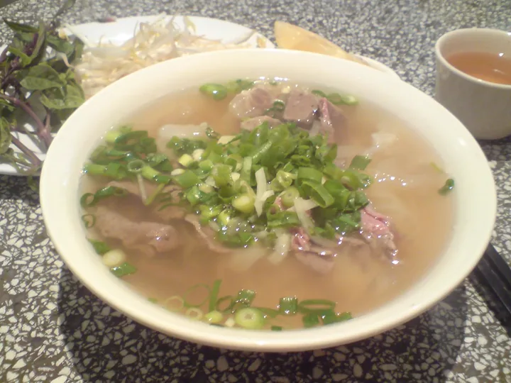A bowl of pho with sliced beef, onion and spring onion