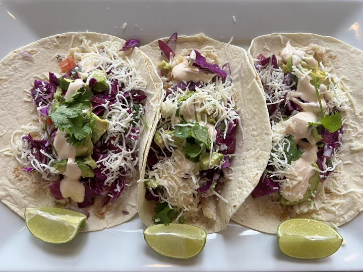 Three soft tacos garnished with herbs and lime wedges