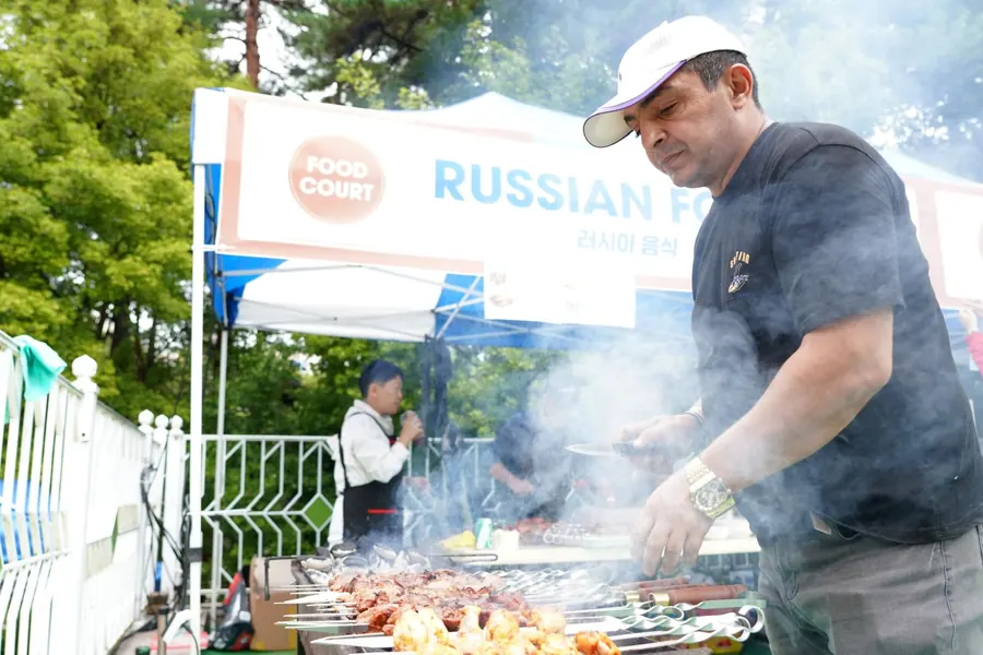 A booth host grilling skewers in a cloud of smoke at the Russian food stall