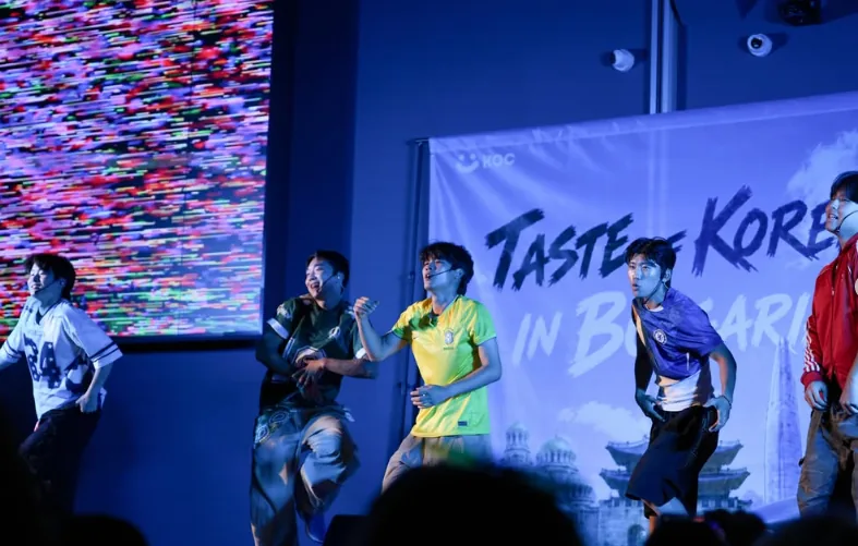 A K-POP dance crew mid-routine in front of a Taste of Korea stage backdrop