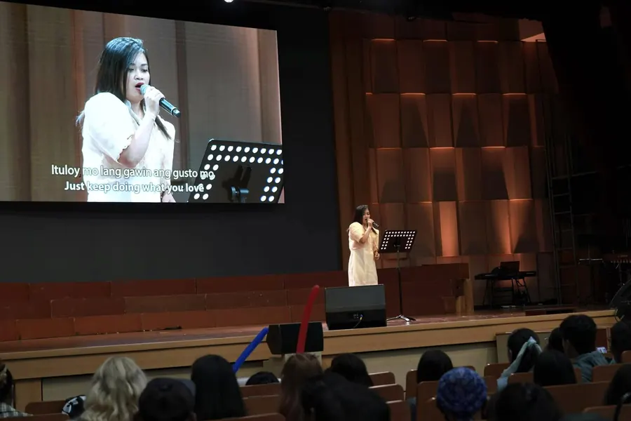 A contestant singing on the main stage with the lyrics shown on screen