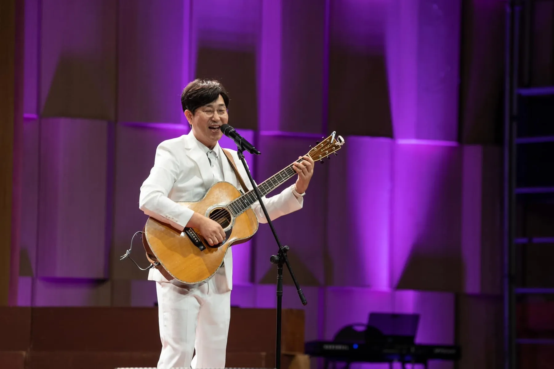 A singer with an acoustic guitar under purple stage lights at the 2024 festival