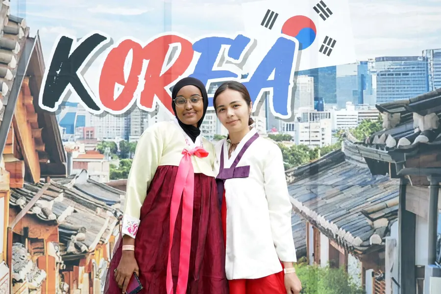 Two participants in hanbok smiling in front of the KOREA photo wall