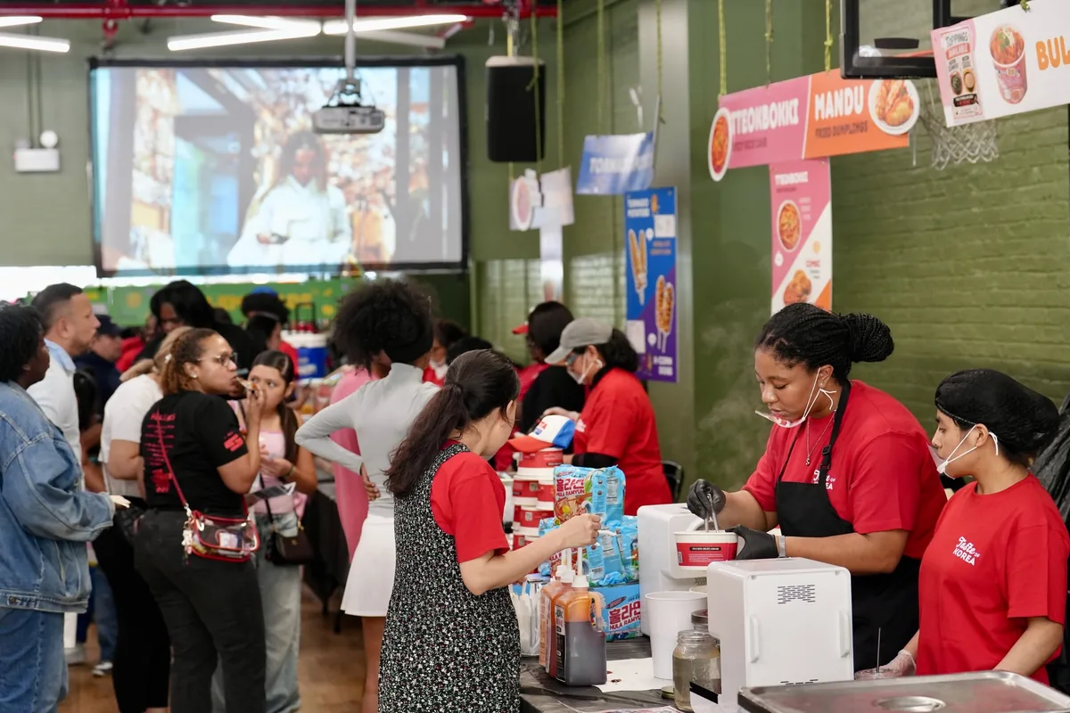 Booth hosts in red aprons serving a queue of visitors at a world food counter